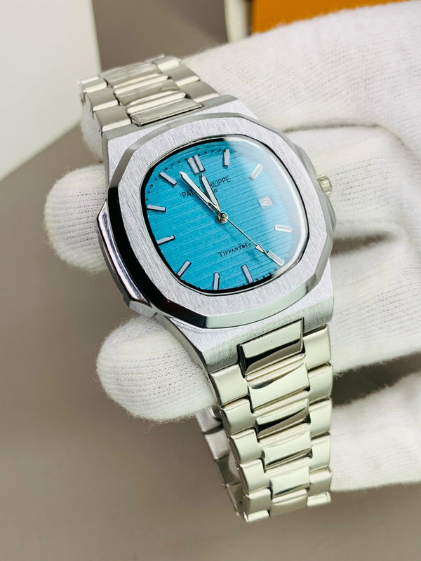 Silver men's luxury wristwatch with blue dial and stainless steel bracelet, held by gloved hand